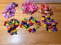 Photo showing six Hawaiian leis arranged on a wooden floor with various bright colored artificial flowers.