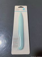 Front view of packed light blue Martha Stewart bone folder tool against grey background.