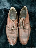 Pair of brown men's dress shoes with brogue pattern, showing top view with laces untied and visible creasing.