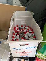 Wide shot of approximately 50 white plastic bottles with red caps inside a Walmart box labeled 'Retourner avec fierte'.