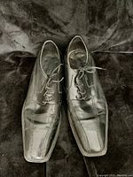 Front view of black leather men's dress shoes with square toe and laces, showing some creasing and wear