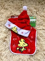 Red Peanuts Christmas baby hat and bib set with white trim, embroidered Woodstock character and festive details.