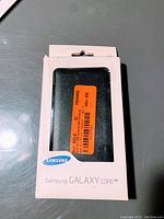 Front of the packaging showing black Samsung Galaxy Core flip wallet case in box with Samsung branding.