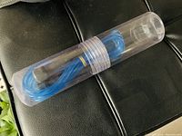 Blue skipping rope coiled inside clear plastic cylindrical container on black surface.