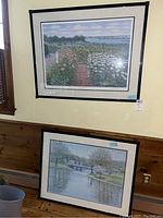 Two framed lithographs on a wall, one above the other showing garden and riverside scenes