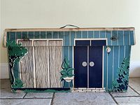 Front view of the Barbie Dream House box showing the illustrated exterior of the house with blue vertical siding and bushes.