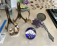 View of the lot showing figurines, blown glass paperweight, wooden picture easels, decorative metal spoon, and purple clay dragon on metal stem.
