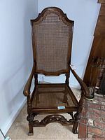 Front view of antique wooden armchair with caned seat and back, visible carved legs and armrests.