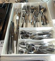 Photo of the various types of cutlery arranged in a white tray organized by knives, forks, large spoons, and small spoons.