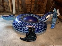 Blue dragon inflatable float displayed in a garage, showing the detailed dragon head with white horns and a blue scaled body.