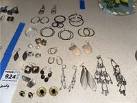 Overview photo of all earrings displayed on a countertop showing variety of styles including hoops, studs, clip-ons, and dangles in silver, gold, and black finishes.