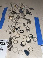 Overall assortment of rings and earrings displayed on a surface with blue tape borders, showing the variety of sizes and styles.