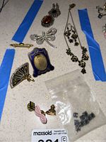 Collection of jewelry including Michael Negrin necklace and earrings, various pins, and single earrings arrayed on a table with blue tape around some items.