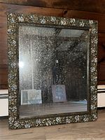 Front view of wood framed mirror showing the ornate floral pattern on the frame and spotting on the mirror glass surface.