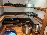 Shelf showing assortment of baking and cooking cookware, including frying pan, cast iron pans, cooling rack, muffin tray, springform cake pan, stainless steel pot with lid and steamer insert.