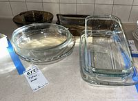 Various glass baking dishes and bowls including clear and amber tinted pieces, stacked dark bowls, and Pyrex/Anchor Hocking ovenware.