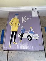 Closed purple metal Ken doll carrying case showing retro artwork on top depicting two male figures and a girl in a car.