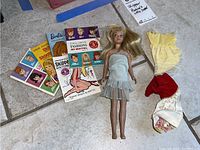 Photo showing vintage Skipper doll, three pieces of clothing, and five Mattel booklets displayed on tile floor.