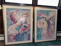 Photo showing two framed and signed prints with foil accents featuring abstract figures in hats and pastel colors
