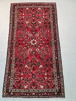 Front full view of rug showing red field with floral and vine pattern and brown border.