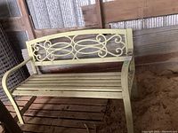 Full view of light green metal bench showing front and side angle with curved scrollwork backrest and slatted seat.