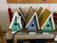 Photo showing all six wooden bird houses lined up on a table, displaying varied pastel colors and roof details.
