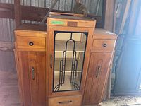 Front view of the wooden Art Deco style cabinet showing center glass door with geometric metal design, and two side drawers and lower cabinets.