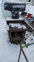 Front view of rusted cast iron stove body with attached flue pipe and snow on top