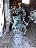 Front view of white metal peacock style chair with floral cushions, showing intricate scrollwork and paint wear.