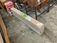 Five boxes of flooring stacked on concrete floor in workshop environment. Each box sealed in plastic packaging with labels visible.