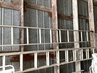 Two long wooden extension ladders with metal bracing leaned against a corrugated metal wall inside a shed. The ladders have multiple rungs and are equipped with ropes and pulleys for adjustment.