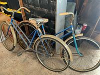 Photo showing side view of two vintage women's bicycles with weathered blue paint and rusty metal parts