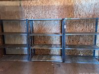 Three shelving units side by side against plywood wall