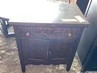 Front view of the wood nightstand showing one drawer with two knobs and two paneled doors with one knob below. The wood finish is dark with a visible grain pattern.