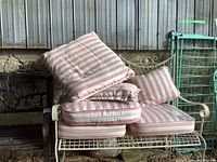 White metal framed outdoor loveseat with several pink-and-white striped cushions stacked on seat