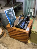 Wooden planter box containing black outdoor lantern fixture parts and a printed instruction sheet.