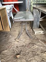 Side view of the outdoor coffee table showing metal legs and rectangular glass top in a dusty environment.