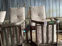 Two beige metal patio chairs with vertical slat backs and padded back cushions, along with matching ottomans on ground. Stored in metal shed with dirt floor.