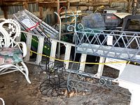 Wide shot showing white ornate chair, black swan shaped metal planter, metal lattice planter box and other garden items in a shed