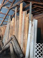 Full view of scrap wood pieces stacked vertically in a shed, including light-colored and unfinished wood planks and cylindrical wooden posts.