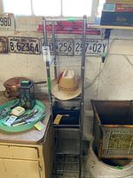 Full view of metal shelving unit next to a cabinet and a decorative planter, with items displayed on shelves including hat and handbag.