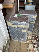 Pair of speakers completely wrapped in bubble wrap with tape, shown standing upright.