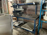 Wide view of the steel workbench table with a scale weight on top, showing rust and staining on the top surface and frame.