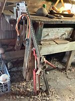Red farm jack with lifting bar and orange straps leaning against workbench, showing ratchet base and condition.
