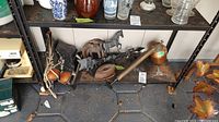 Wide view of the lot showing iron horse weathervane, vintage skates, sad iron, horseshoes, and vintage metal sprayer on a shelf.