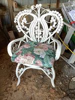 Front view of white wicker armchair with floral cushion, showing ornate spiral patterns on backrest.