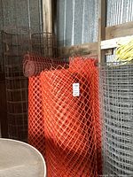 Rolls of orange plastic mesh fencing, metal wire fencing, and yellow rope visible in a corrugated metal shed.