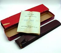 Red storage box, brown leather case, Hughes Owens Versalog 1771 slide rule, and original 1952 instruction booklet on white background