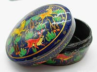 Top and side view of a round black lacquer box with colorful hand-painted wild animals including tigers and deer on blue background with green foliage and gold outlines. Visible vintage wear on edges.