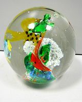 Clear glass spherical paperweight showing green turtle and red and green fish figurines with white bubble elements.